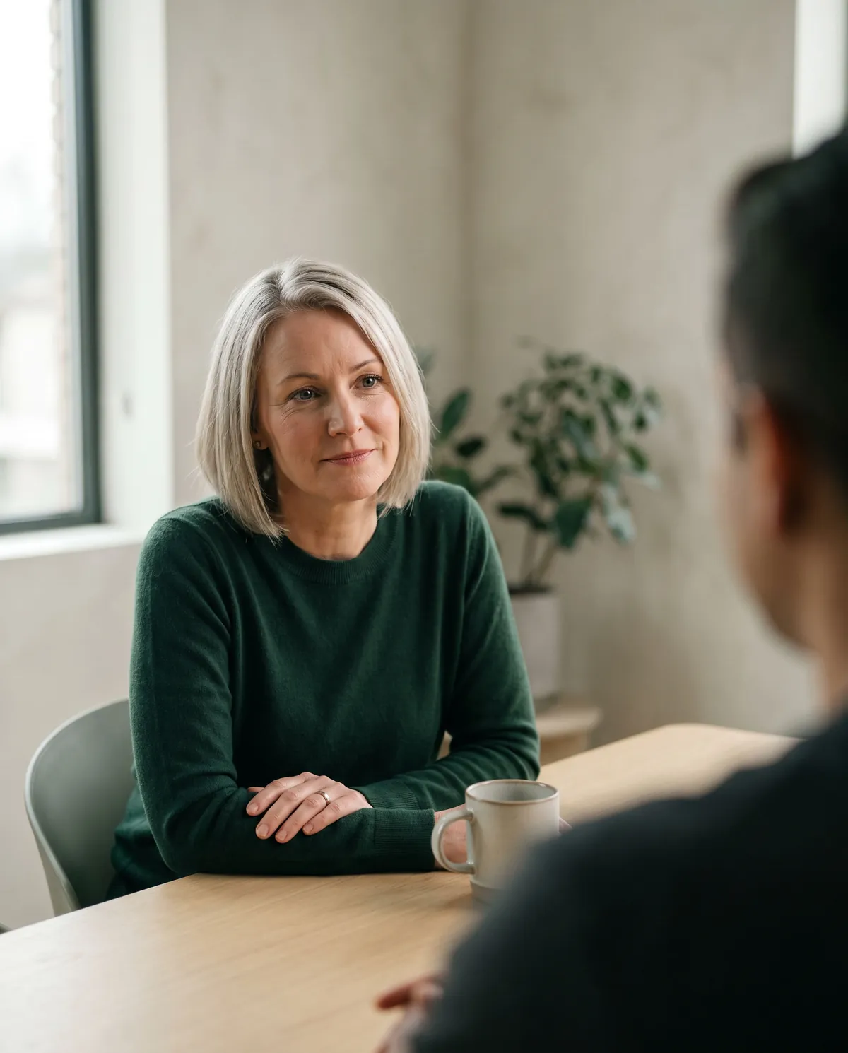 A bookkeeper listens closely to a client across an oak table, hands folded beside a mug.