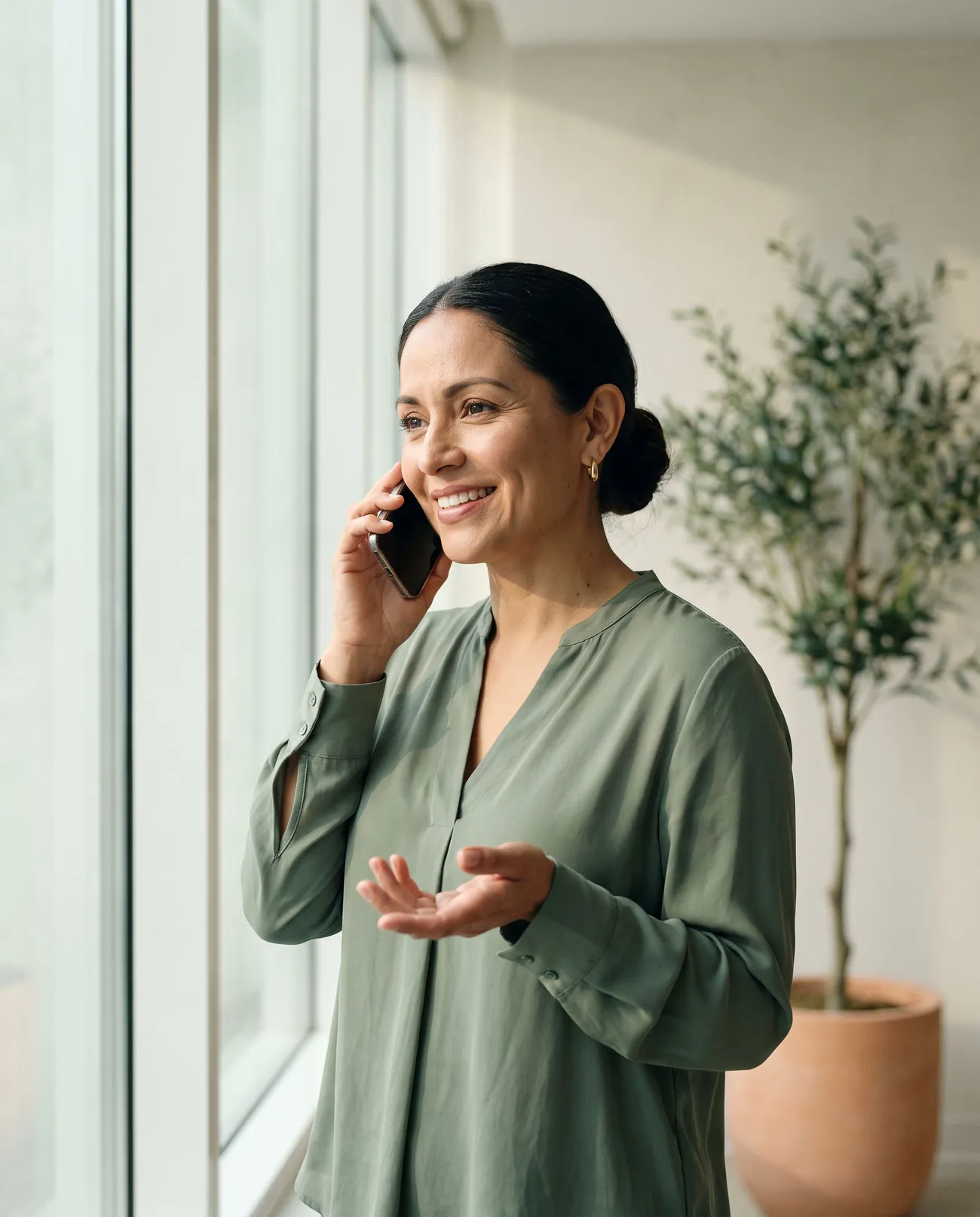 A bookkeeper by a window explains something on a phone call with a warm smile.